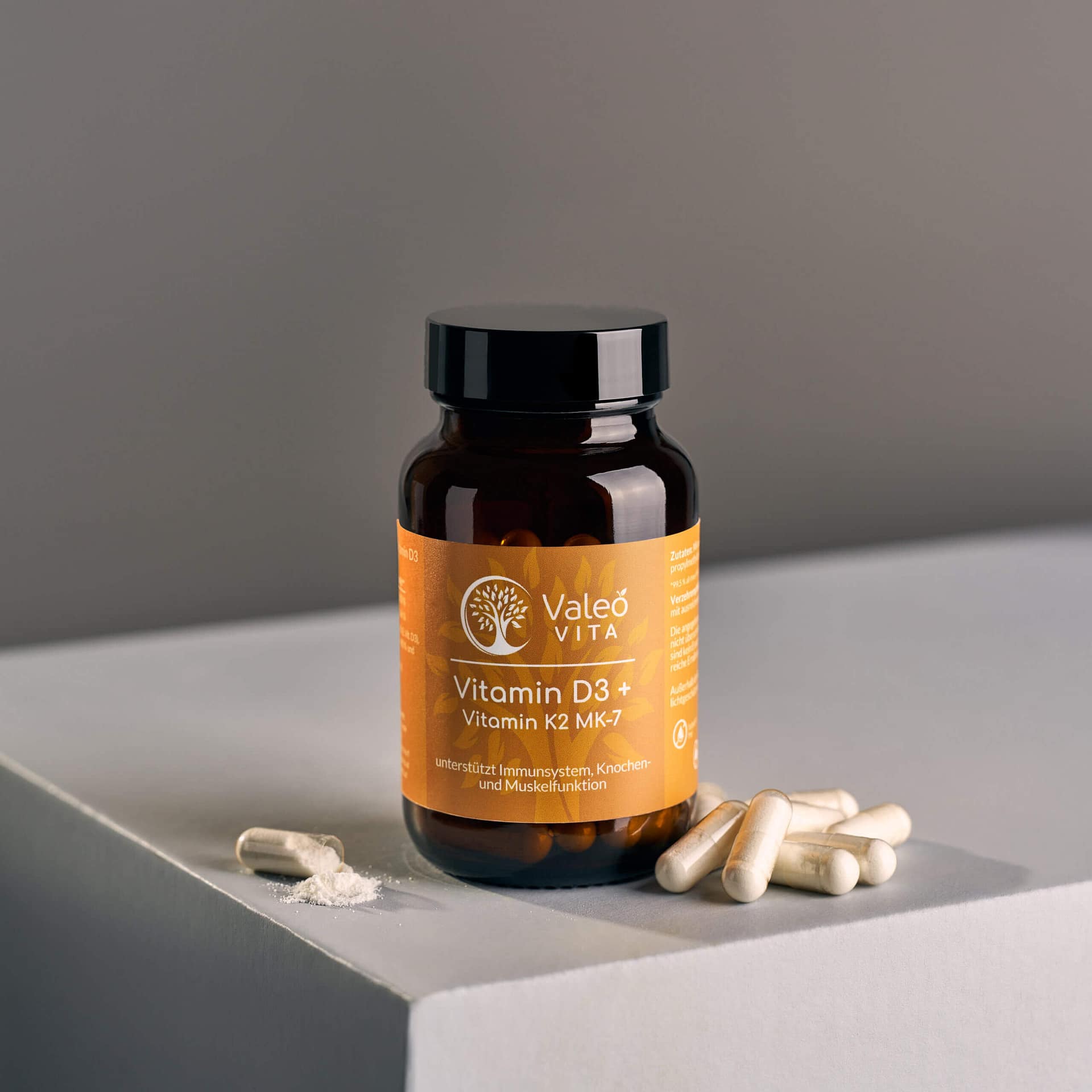 Valeo Vita Vitamin D3 und Vitamin K2 MK-7 Kapseln in Braunglasflasche mit geöffneten Kapseln auf neutralem Hintergrund